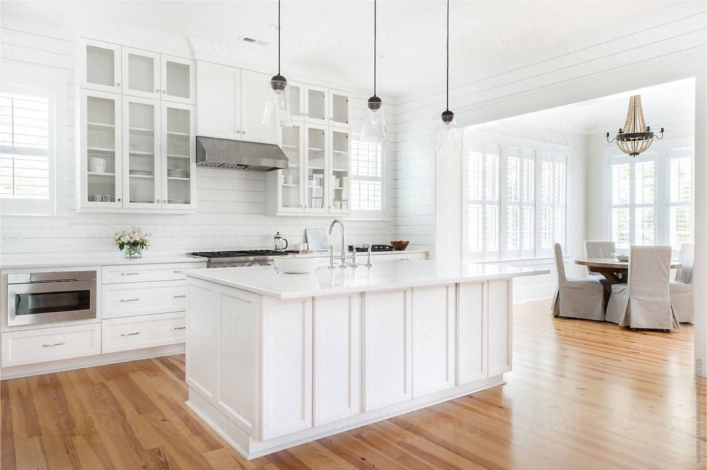 A modern, bright white kitchen with stainless steel appliances, white granite counter tops and bright, hardwood floor